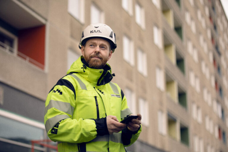 Byggperson står på projekt med arbetsorder och tidsrapport i mobilen